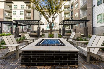 an outdoor patio with a firepit and chairs and an apartment building at The Monroe Apartments, Texas, 78741